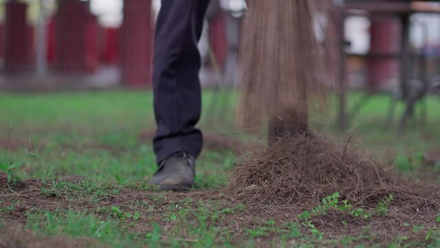 A worker is sweeping the yard using a coconut broom stick
