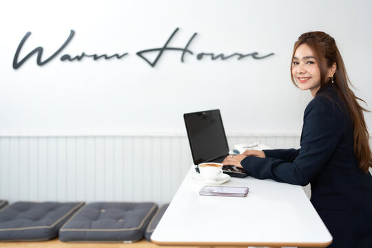Asian female investor as executive Working in a cafe is relaxed and happy, wearing a suit, using a laptop to check on company business systems while sipping delicious coffee.