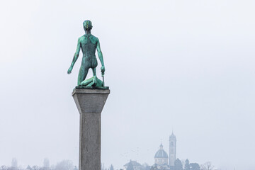 Statue of David in a public park in Zurich. In the misty background, diffuse contours of churches