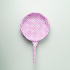 Frying pan packaged in pink polka dot gift paper on a blue pastel background. Creative concept for a woman's gift.