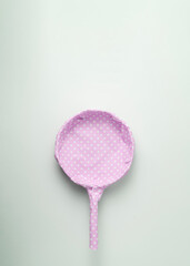 Frying pan packaged in pink polka dot gift paper on a blue pastel background. Creative concept for a woman's gift.