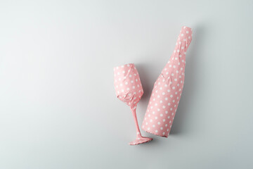 Champagne bottle with glass packaged in pink polka dot gift paper on blue pastel background with...