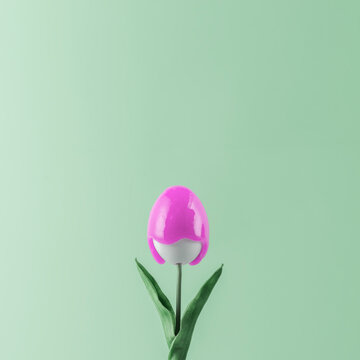 Creative Easter concept. Tulip with a bud in the form of an Easter egg with pink paint flowing down it on a green pastel background.