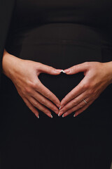 Close up photo of pregnant woman which makes heart shape with hands on pregnant belly.