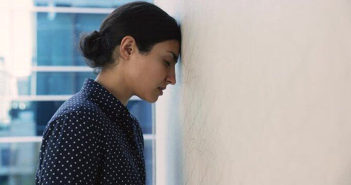 Indian employee, business woman banging her head against wall looks desperate, feel upset due to stressful situation at work, problems, professional failure. Unsuccess, failed job interview, dismissal