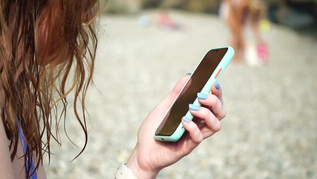 Woman with smartphone. Close-up of woman's hands holding vertical mobile phone and swiping up finger application page against background of sea and beach