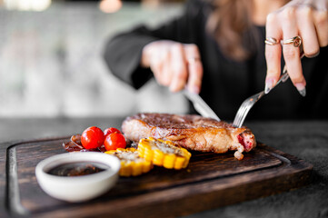 A close-up view of a person slicing into a well-cooked grilled steak served with corn on the cob...