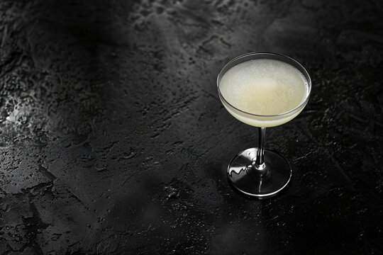 Black and white photo of a frothy cocktail in a coupe glass on a dark textured surface. Monochrome beverage concept for design