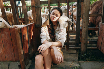 A woman is sitting in front of a herd of sheep in an enclosed area with her hands on her knees