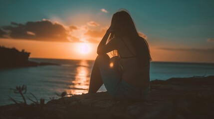 a woman sitting on a rock looking out at the ocean with the sun setting over the ocean in the background.