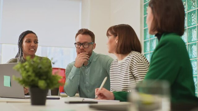 Tracking shot of diverse group creative designers cooperating at office conference room sitting desk. Startup business team discussing work project at boardroom. Focused coworkers brainstorming ideas