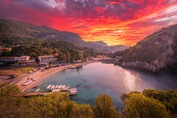 Dramatic sunset skies ignite over Paleokastritsa emerald bay, showcasing the mesmerizing natural...