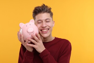 Fototapeta na wymiar Happy man with piggy bank on yellow background