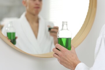 Young man using mouthwash near mirror in bathroom, closeup