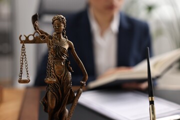 Notary reading book at table in office, focus on statue of Lady Justice and pen