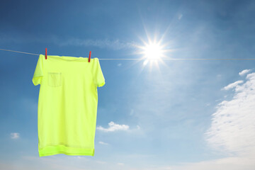 Light green t-shirt drying on washing line against blue sky