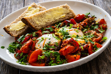 Shakshuka - fried eggs with vegetables on wooden table
