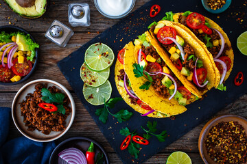 Tacos with ground beef, avocado, corn and fresh vegetables on wooden table
