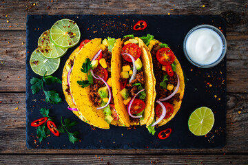 Tacos with ground beef, avocado, corn and fresh vegetables on wooden table
