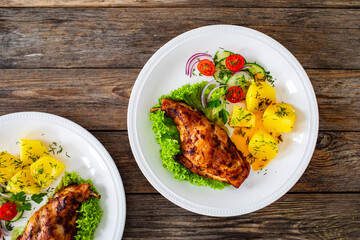 Cooked rabbit thighs with potatoes and fresh vegetable salad on wooden table 