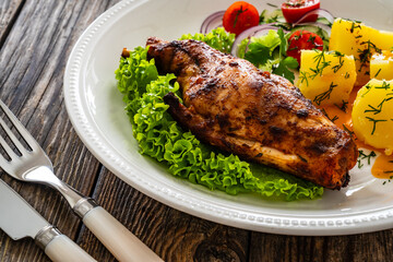 Cooked rabbit thighs with potatoes and fresh vegetable salad on wooden table

