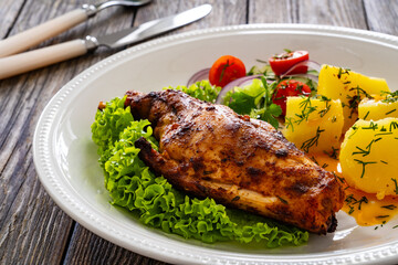 Cooked rabbit thighs with potatoes and fresh vegetable salad on wooden table
