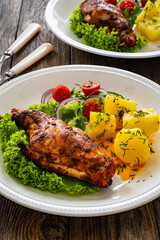 Cooked rabbit thighs with potatoes and fresh vegetable salad on wooden table
