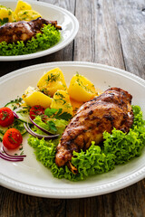 Cooked rabbit thighs with potatoes and fresh vegetable salad on wooden table
