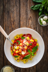 Gnocchi alla sorrentina - gnocchi with melted mozzarella cheese in tomato sauce and Parmigiano Reggiano on wooden table
