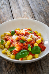 Gnocchi alla sorrentina - gnocchi with melted mozzarella cheese in tomato sauce and Parmigiano Reggiano on wooden table
