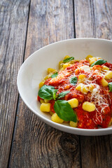 Gnocchi alla sorrentina - gnocchi with melted mozzarella cheese in tomato sauce and Parmigiano Reggiano on wooden table
