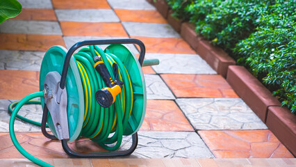 The old water hose reel agriculture accessory with nozzle on stone pavement tile floor in home...