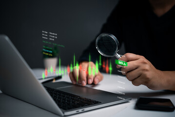 A person examines stock market indicators on a laptop screen using a magnifying glass. The focus on specific data points suggests a detailed analysis of market trends.