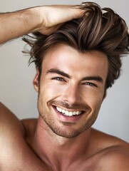 A portrait of a handsome smiling young man, adjusting his stylish hair with his hands. Men's grooming concept