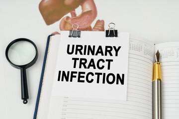 On the table there is a magnifying glass and a notepad with the inscription - Urinary tract infection - obrazy, fototapety, plakaty