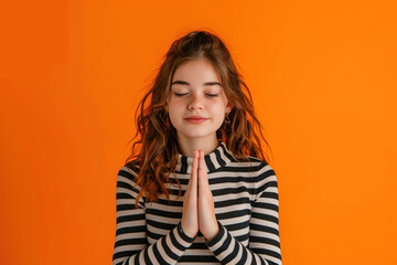 A girl is praying in front of an orange background