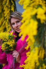 elegant woman in a pink coat stands next to a showcase of decorated mimosa