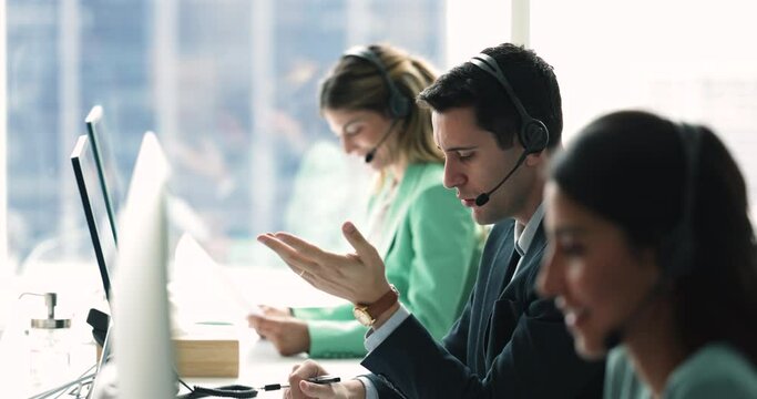 Workflow of call center employees, focus on young Hispanic man wear headset, provide customer service, support through call in callcenter office, consider inquiries, resolve issues of company clients