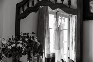 Wedding preparation, dress hanging on window, flowers.
