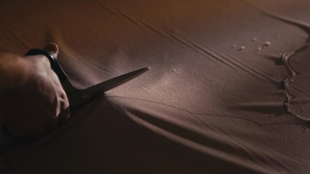 Close-up of a hand skillfully cutting fabric with sharp scissors in a dark workshop. This precision tool is used in garment making and furniture industry, showcasing the art of textile craftsmanship.