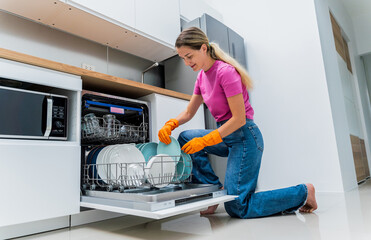 Young woman takes dishes out of the dishwasher machine