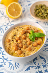 A bowl of hummus with chickpeas and basil on a table
