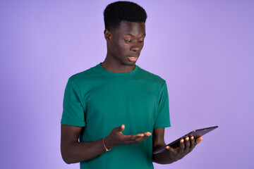 Young black man doing a video conference with a tablet with violet background for copyspace.