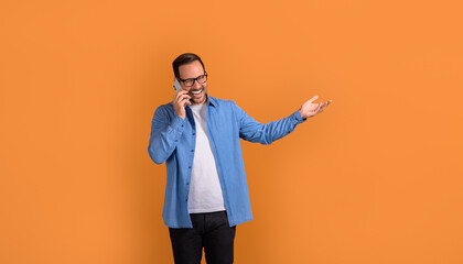 Portrait of happy handsome professional gesturing and talking over mobile phone on orange background