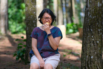 Asian woman sitting alone on a log in the park, eating tasteless fried banana