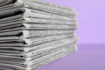 Stack of newspapers on light violet background, closeup. Journalist's work