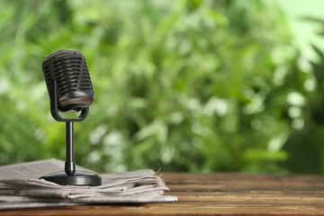 Newspapers and vintage microphone on wooden table against blurred green background, space for text....