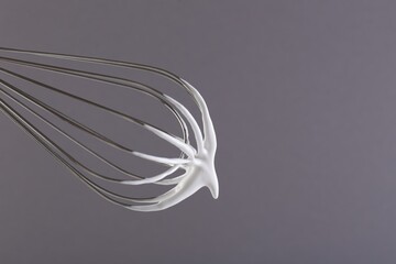 Whisk with whipped cream on grey background, closeup. Space for text