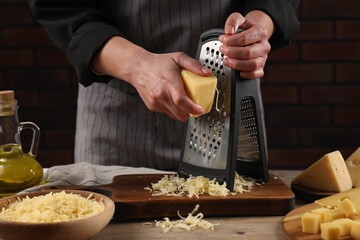 Woman grating cheese at wooden table, closeup