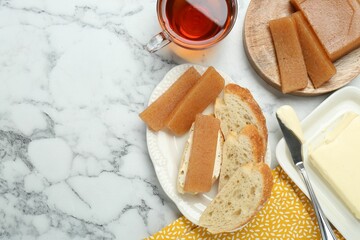 Delicious quince paste, bread, butter and cup of tea on white marble table, flat lay. Space for text